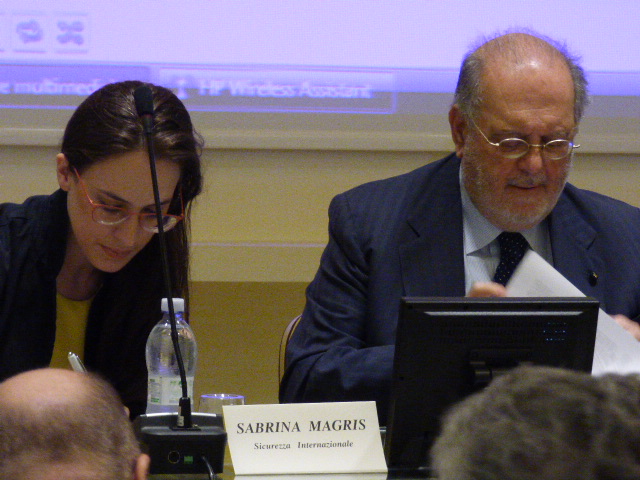 Due relatori al tavolo di una conferenza, con il cartellino dei nomi davanti.