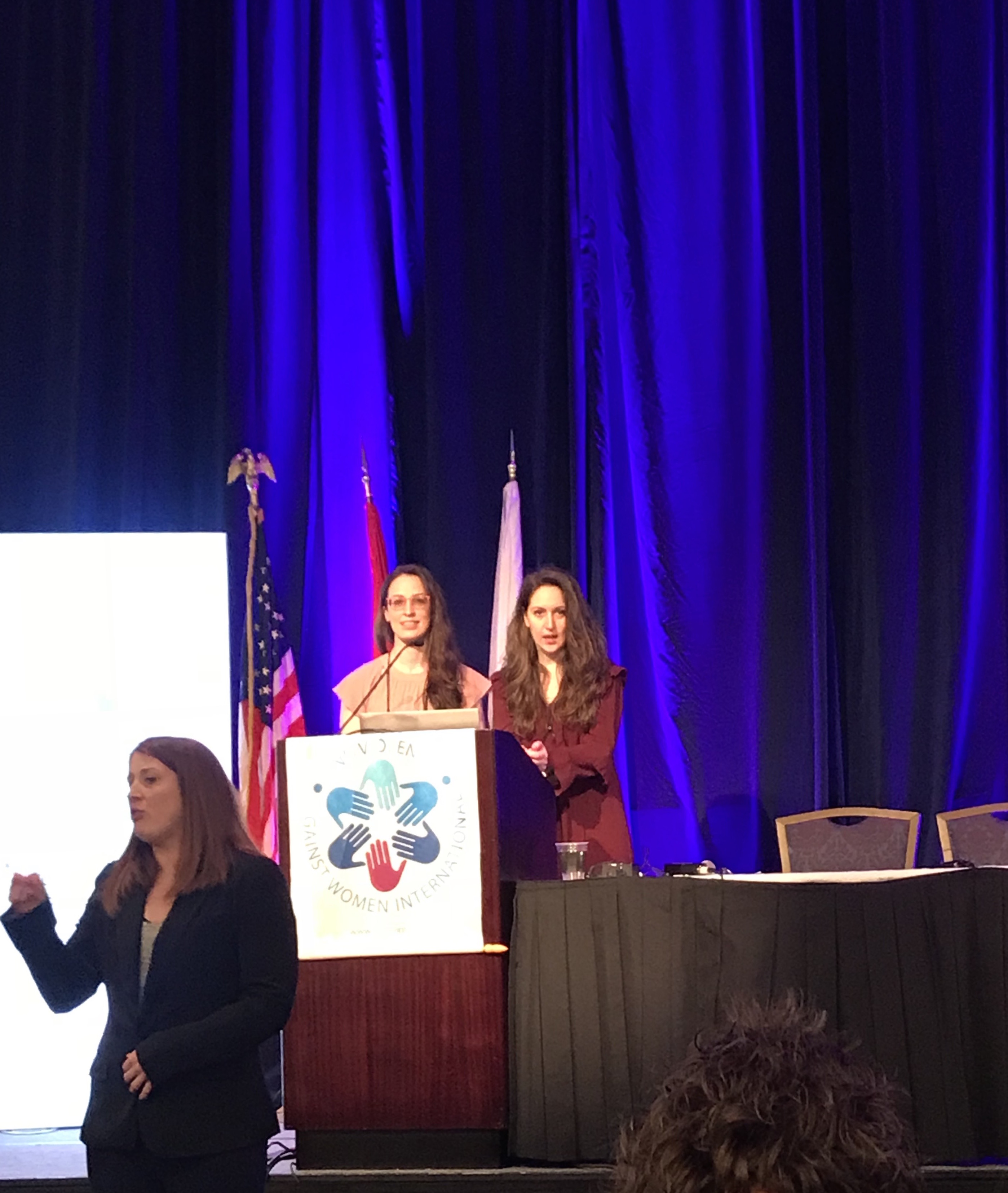 Due relatrici al podio di un congresso, accanto a un'interprete della lingua dei segni.