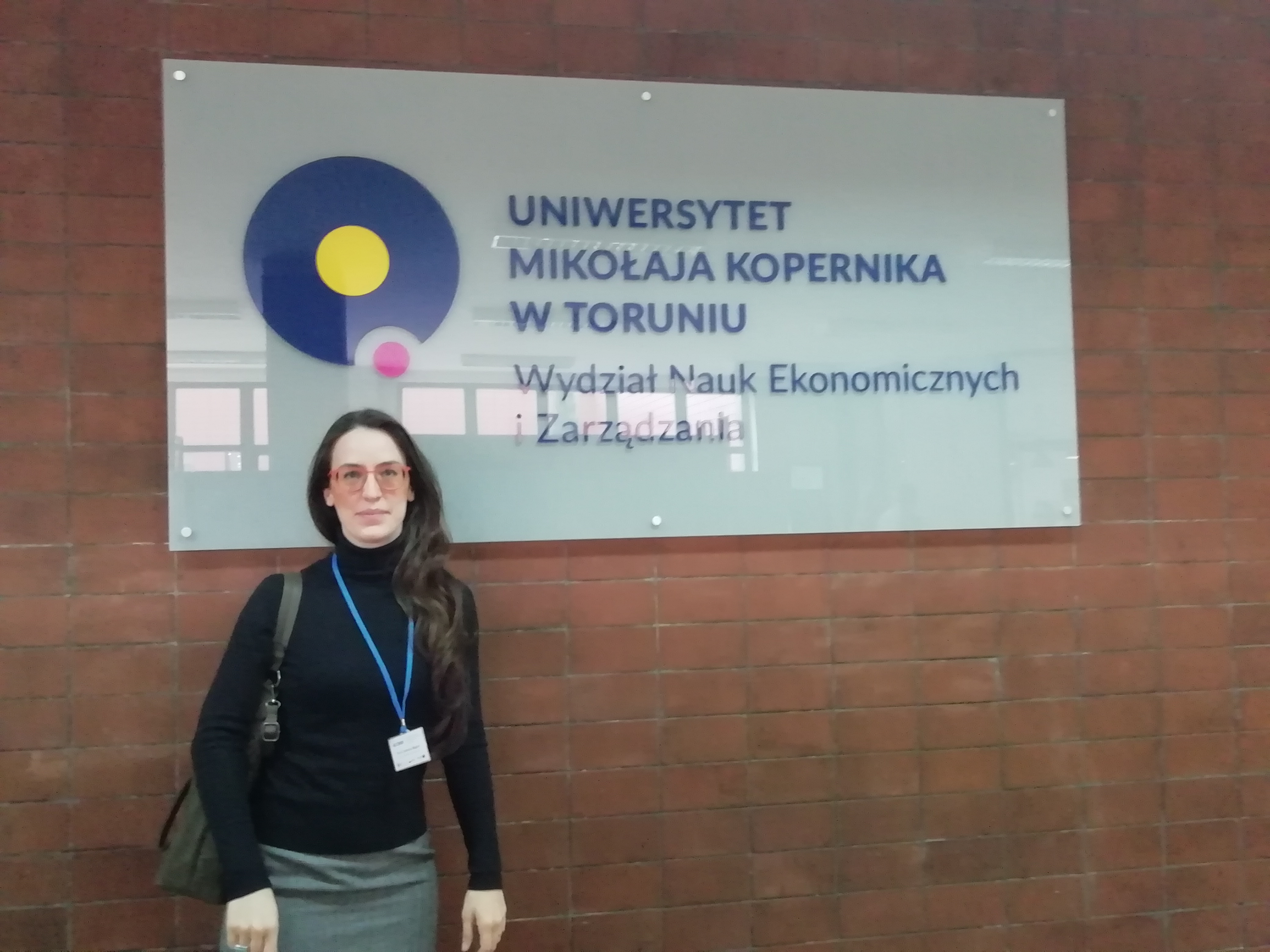 Una partecipante col badge davanti all'insegna dell'Università Niccolò Copernico di Toruń, facoltà di scienze economiche e gestione.