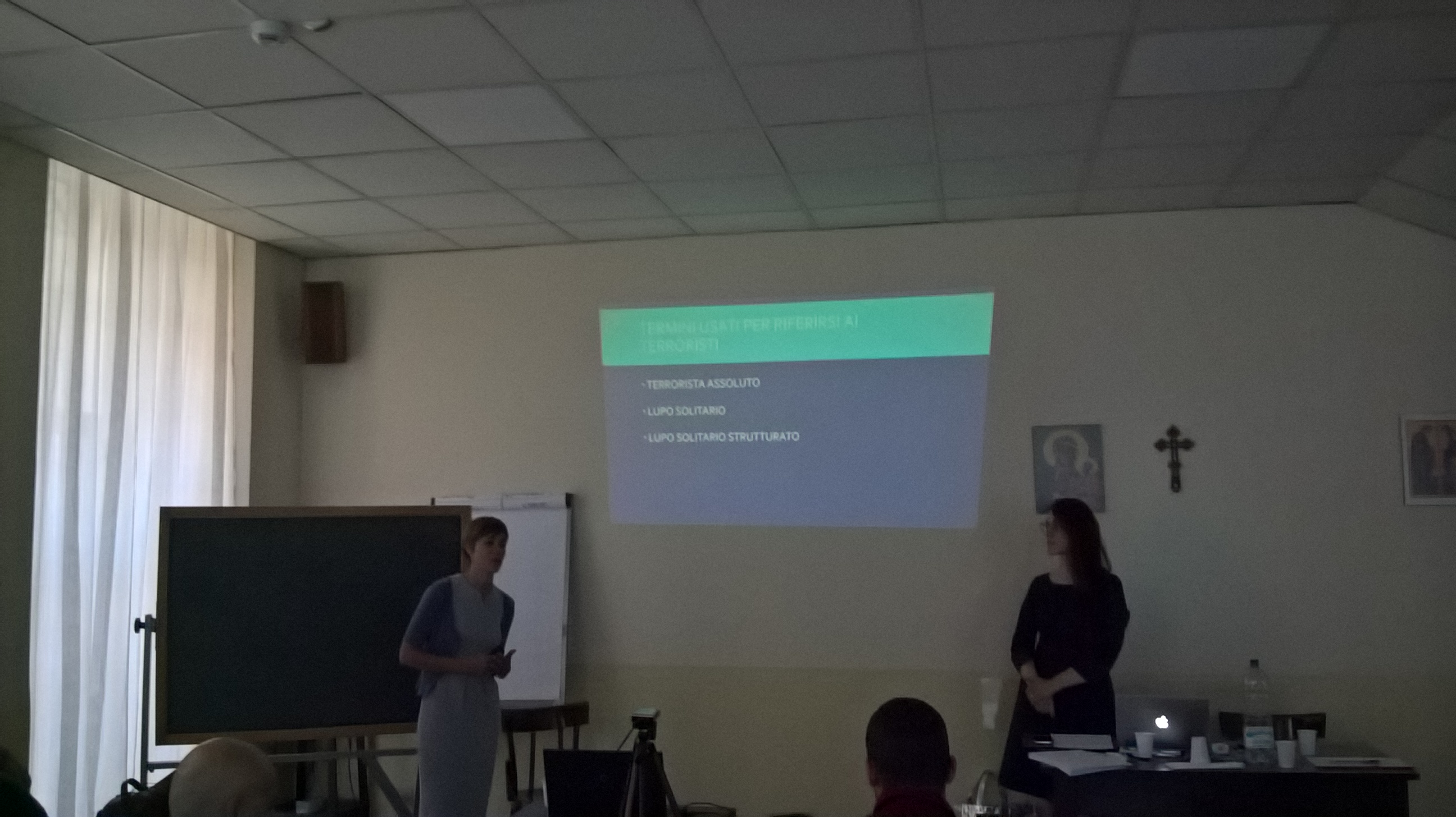 Due relatrici ai lati dello schermo durante una lezione, in una sala chiara.
