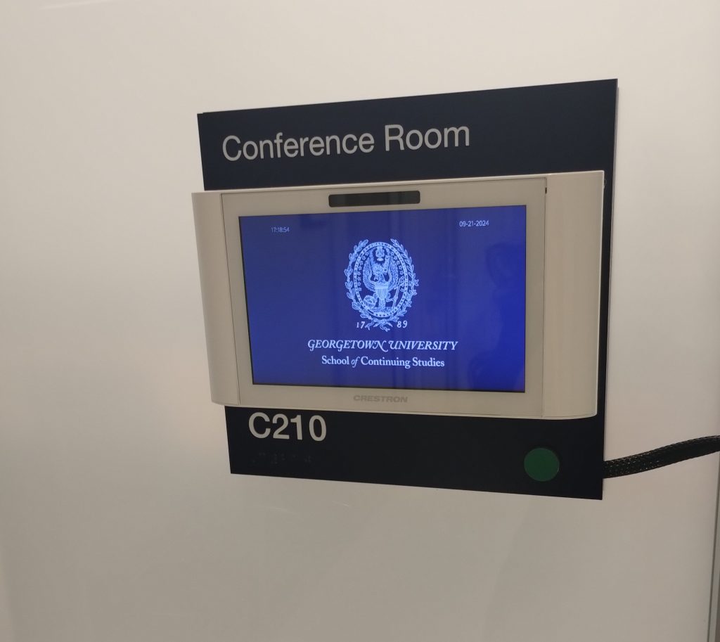 Il pannello di una sala riunioni con lo schermo che mostra il sigillo della Georgetown University, School of Continuing Studies, sala C210.