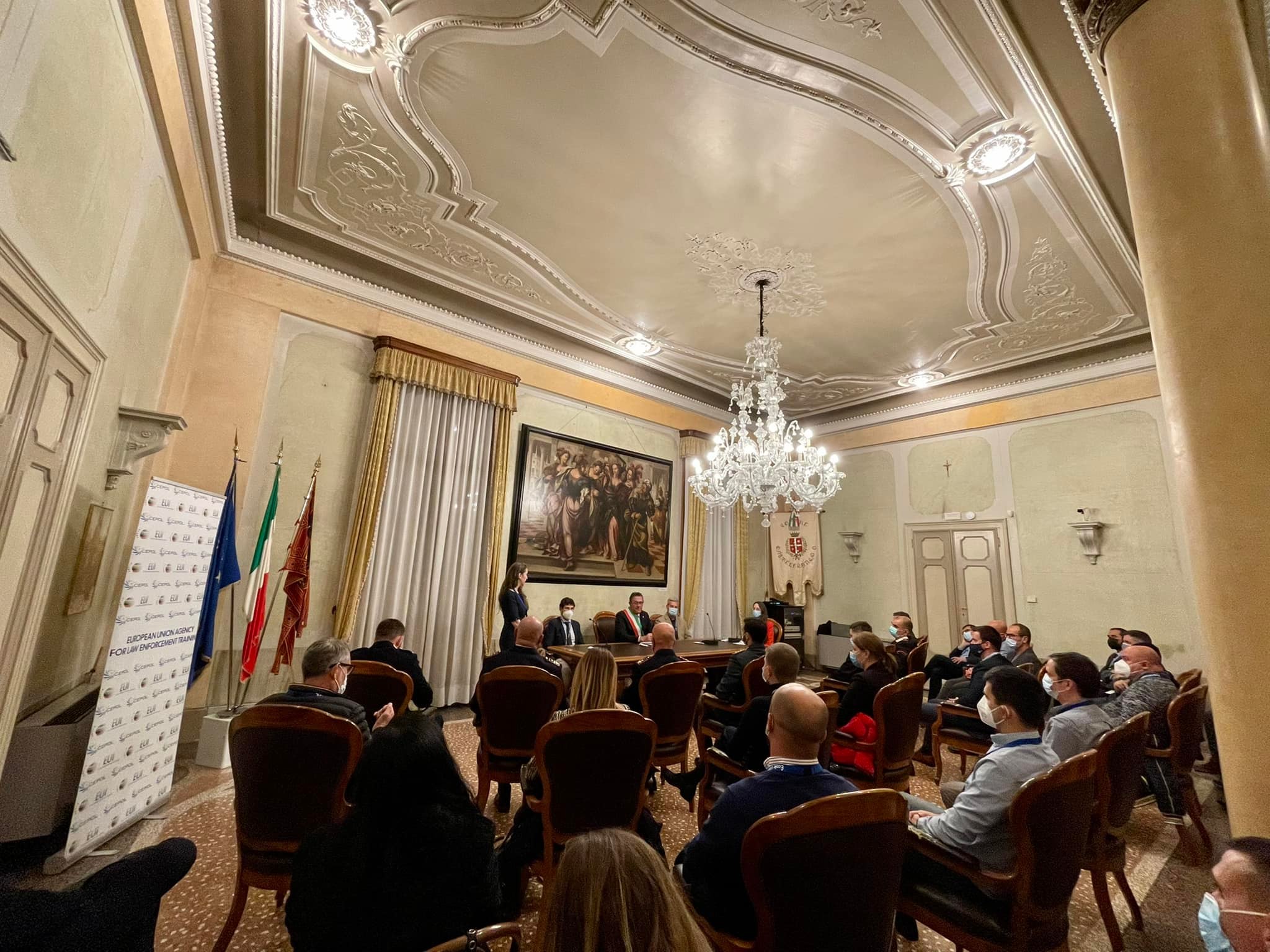 Una sala storica con il soffitto a stucchi e il lampadario di cristallo: il pubblico seduto e il tavolo dei relatori in fondo.