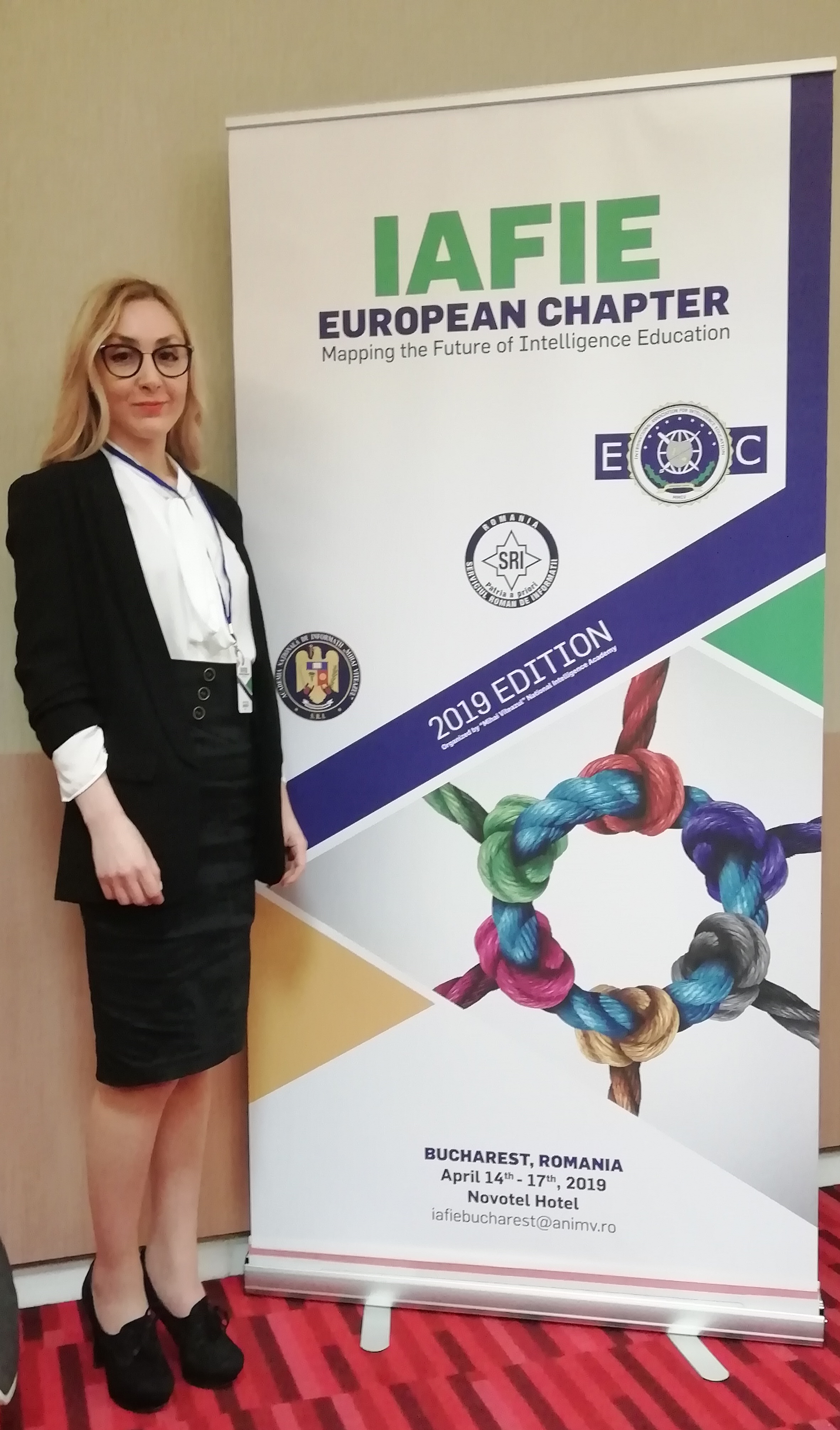 Una partecipante in posa davanti al banner IAFIE European Chapter, Mapping the Future of Intelligence Education, edizione 2019, Bucarest.