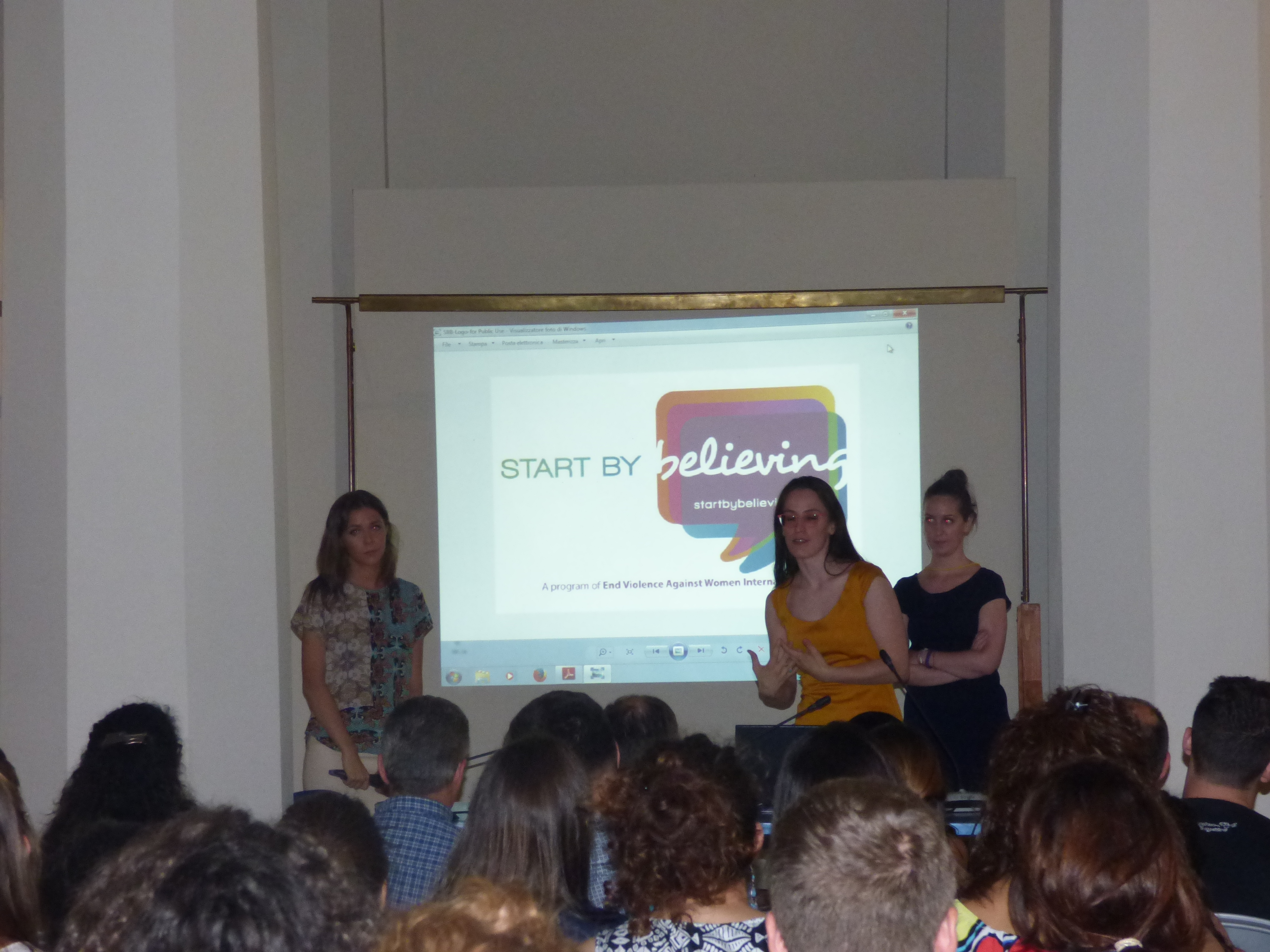 Tre relatrici davanti alla proiezione del logo della campagna Start by Believing.