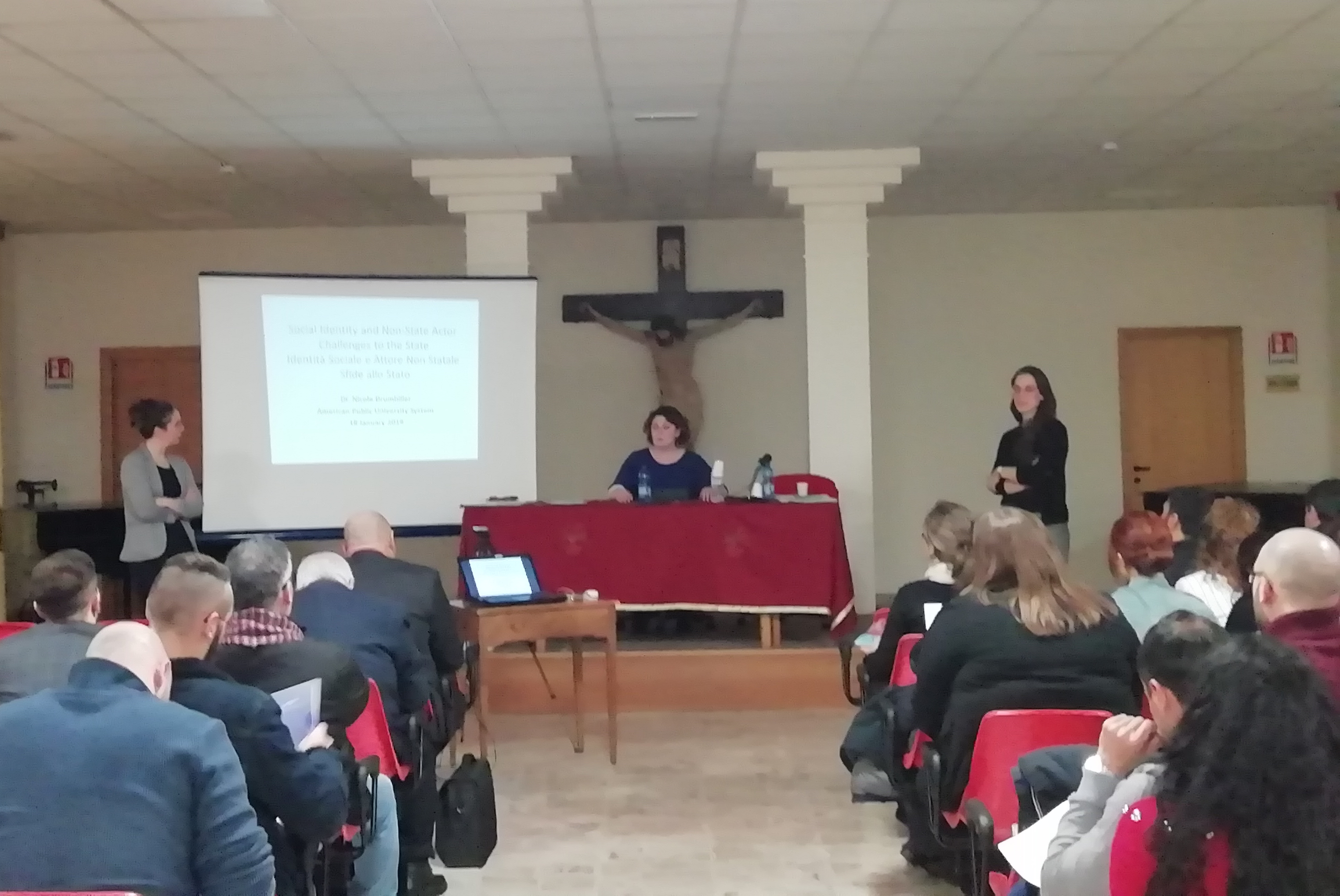 Tre relatrici davanti al pubblico seduto: una allo schermo, una al tavolo e una in piedi.
