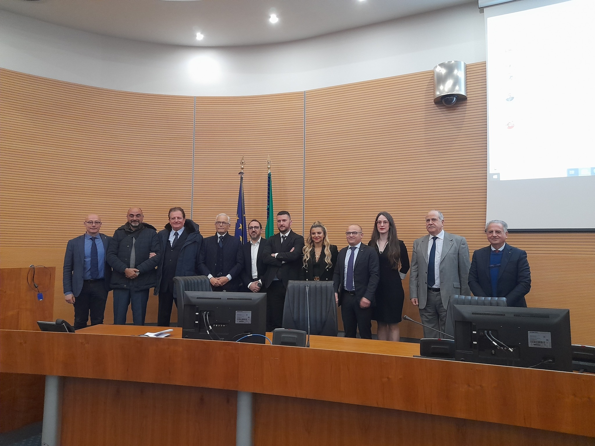 Undici persone in posa nell'emiciclo di un'aula, davanti alle bandiere.