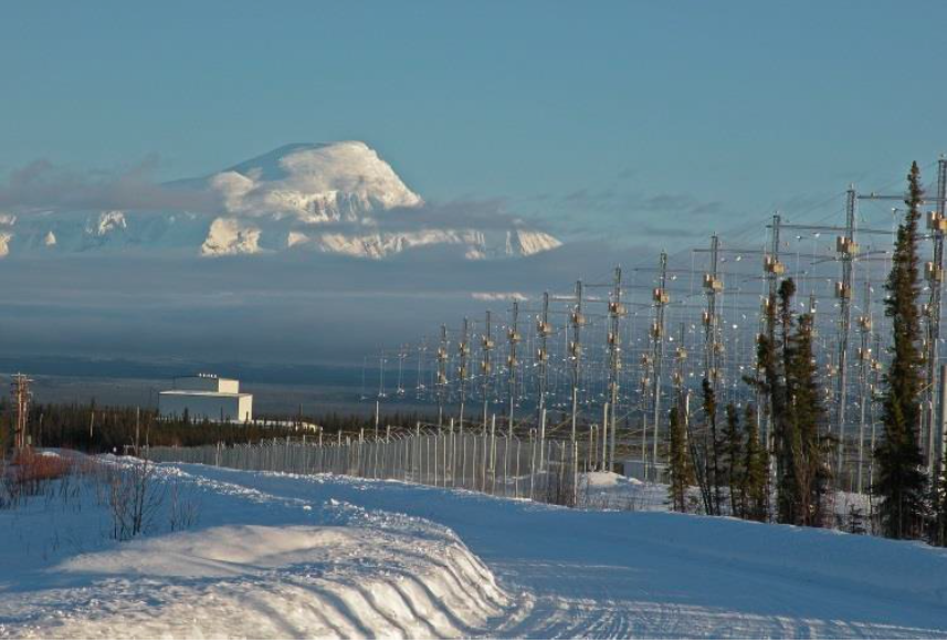 Un campo di antenne innevato, con una montagna sullo sfondo e un edificio bianco fra gli abeti.