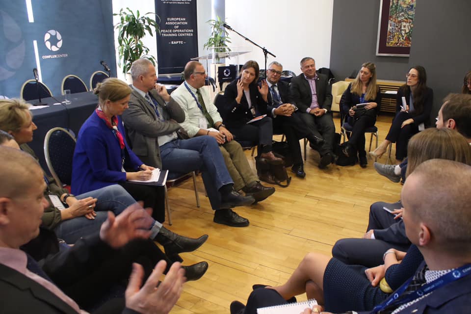 I partecipanti seduti in cerchio durante una discussione, con il banner della conferenza alle spalle.