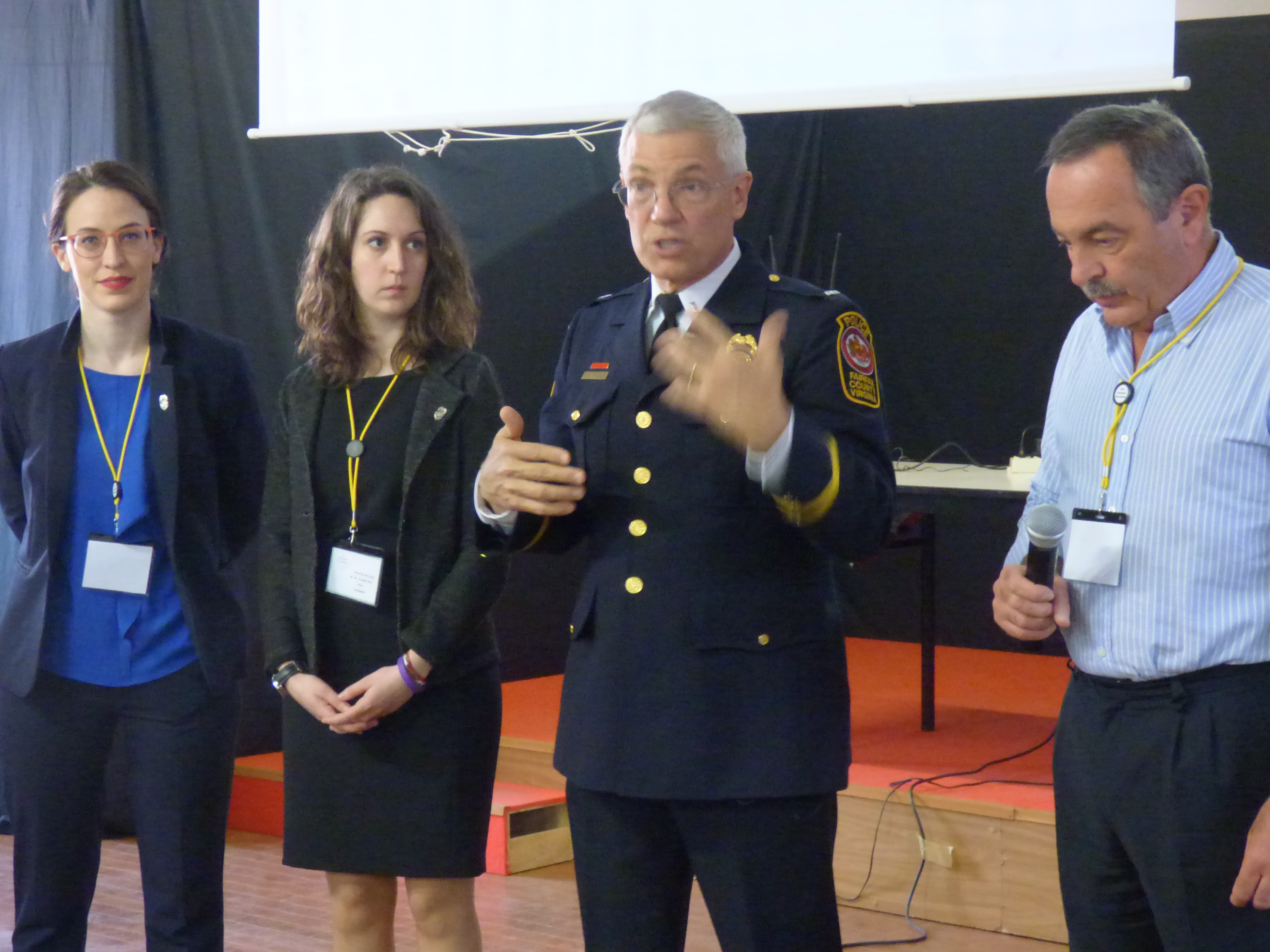 Quattro persone in piedi: due relatrici, un ufficiale di polizia statunitense in uniforme che parla, e un uomo col microfono.