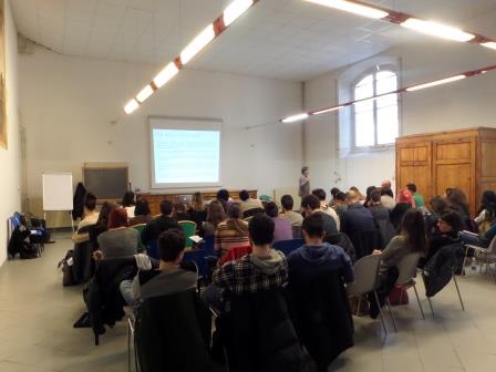 Un'aula piena vista da dietro, con la proiezione delle diapositive in fondo alla sala.
