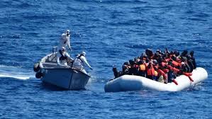 Un gommone carico di persone in mare aperto, affiancato da una motovedetta.