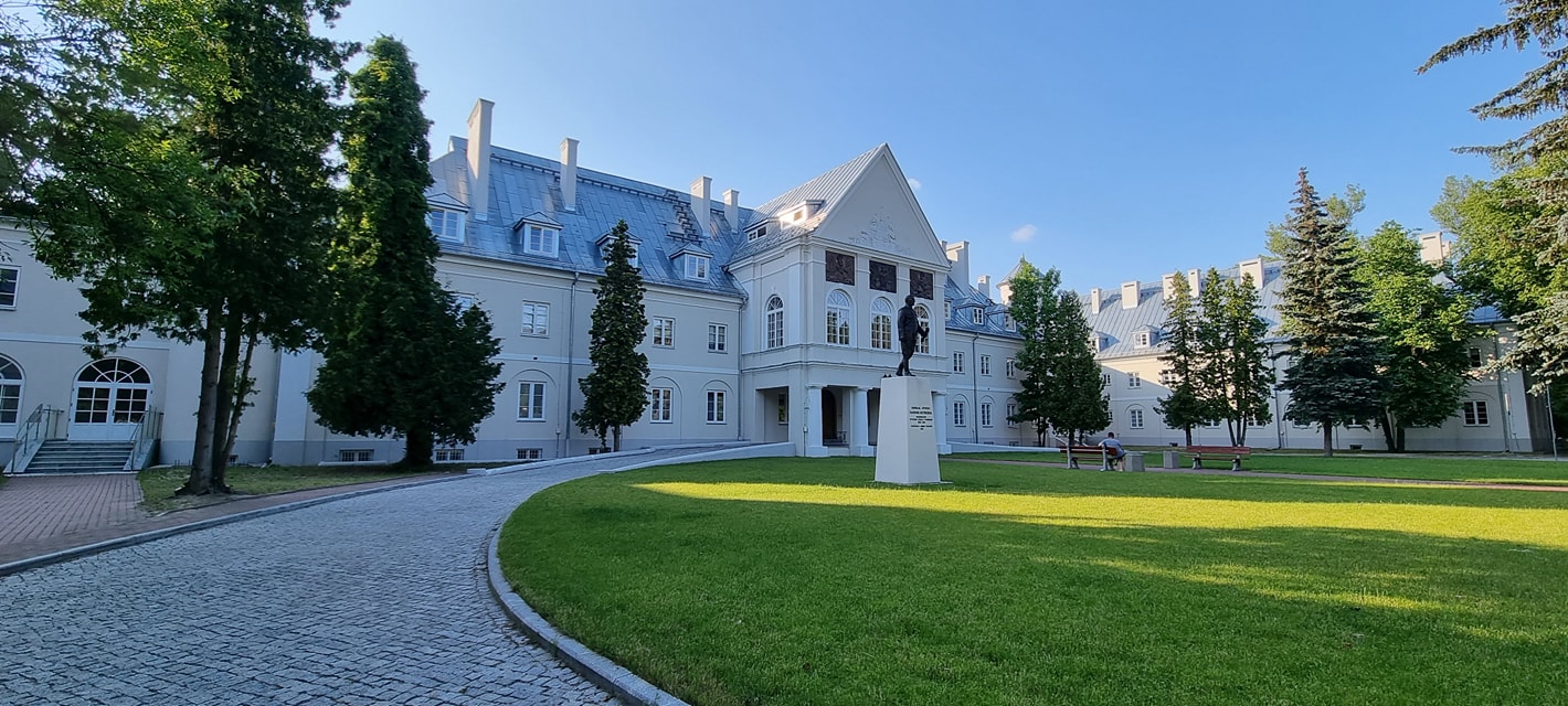 Un palazzo storico bianco visto dal parco, con il vialetto e un monumento davanti all'ingresso.
