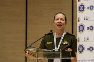Una relatrice in uniforme parla dal podio, davanti al fondale con i loghi EUI.