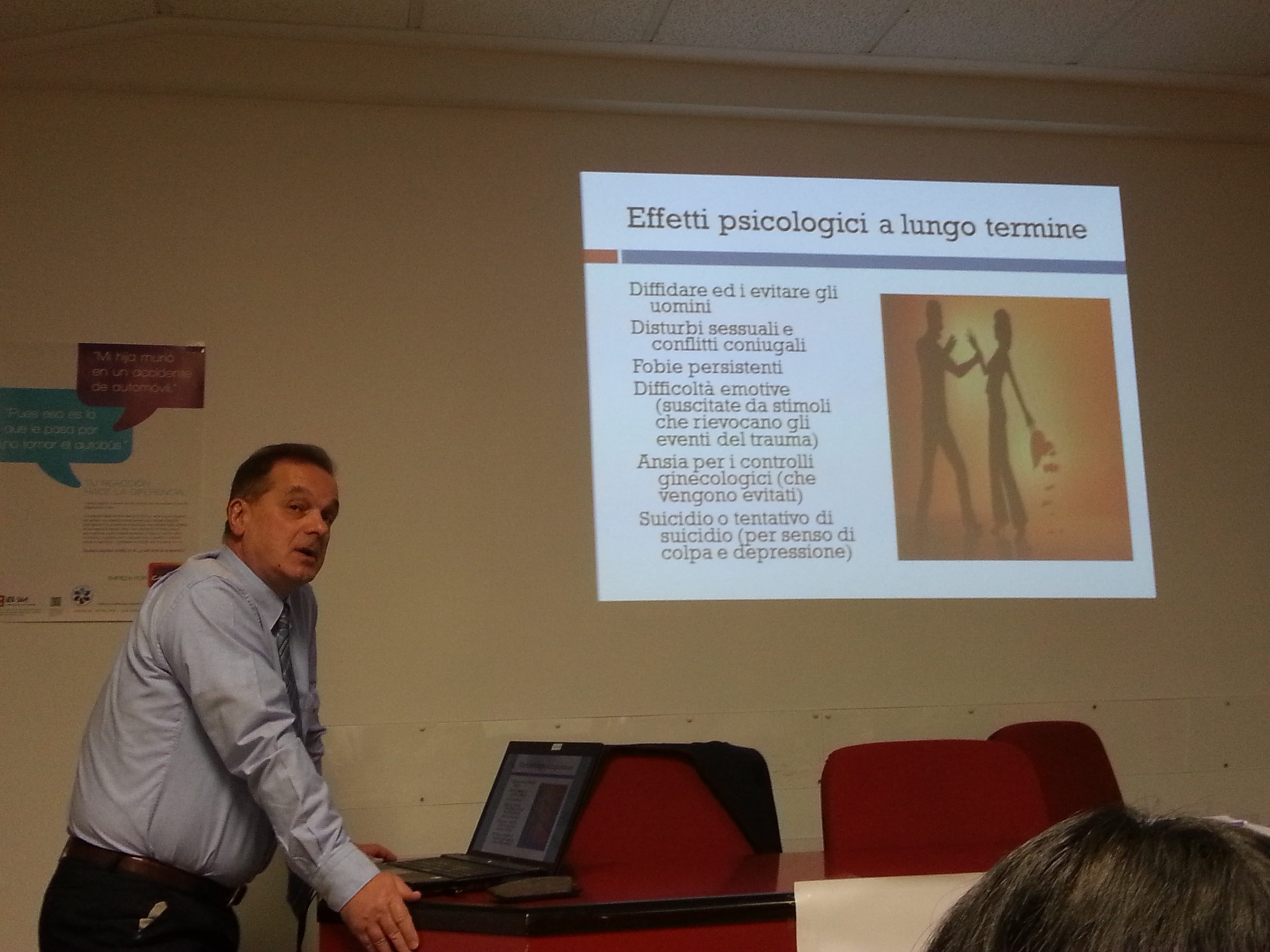 Un relatore accanto alla proiezione di una diapositiva sugli effetti psicologici a lungo termine.