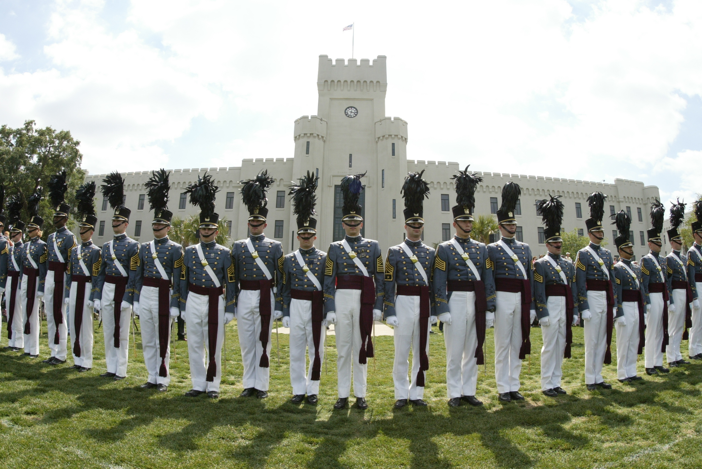 Cadetti schierati in uniforme di gala sul prato davanti a un edificio con le torri merlate.