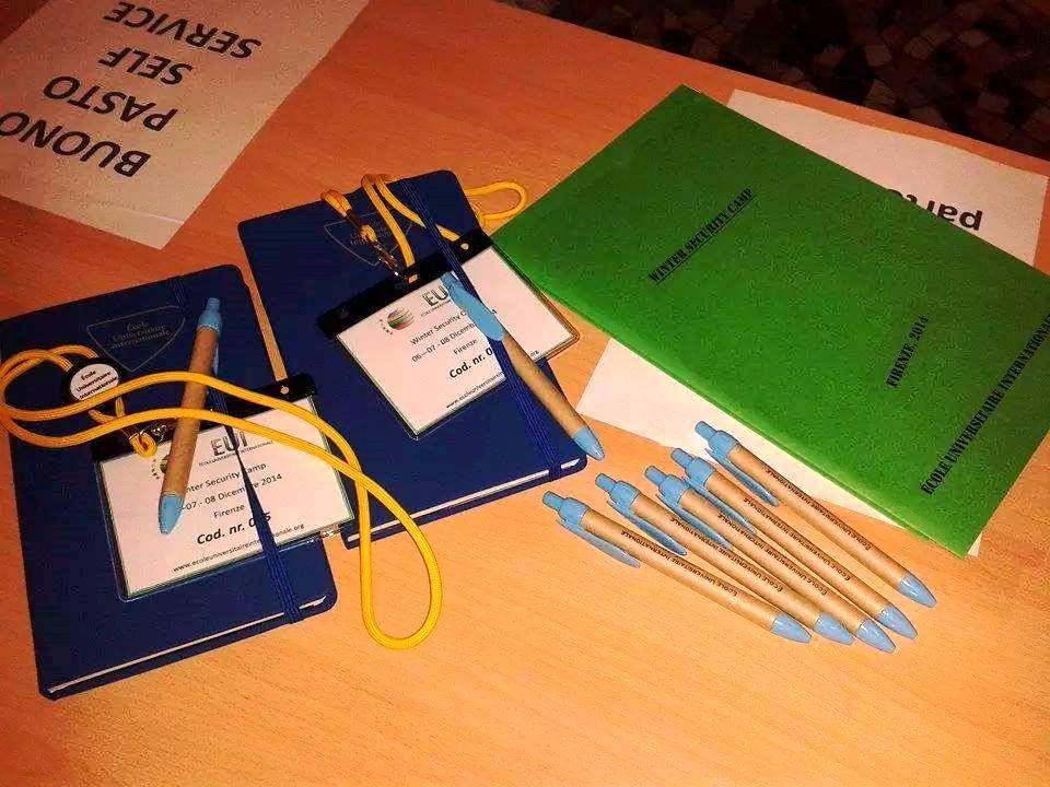 Il materiale dei partecipanti: taccuini blu e verde con il logo dell'istituto, cordini gialli, badge e penne.