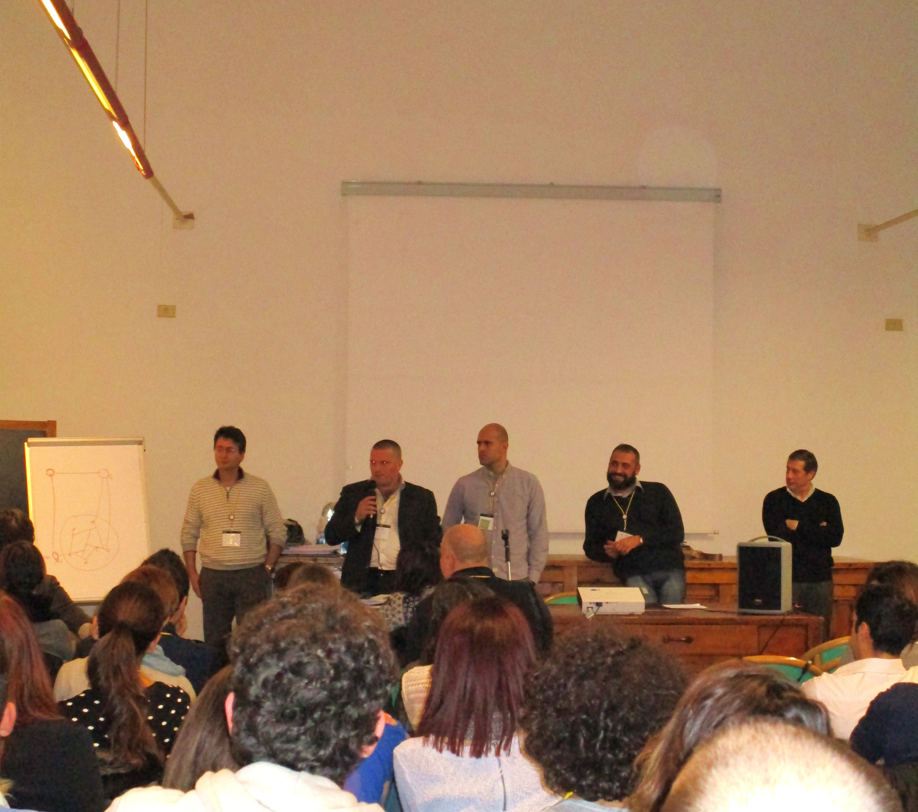 Cinque relatori in piedi davanti all'aula; uno parla al microfono.
