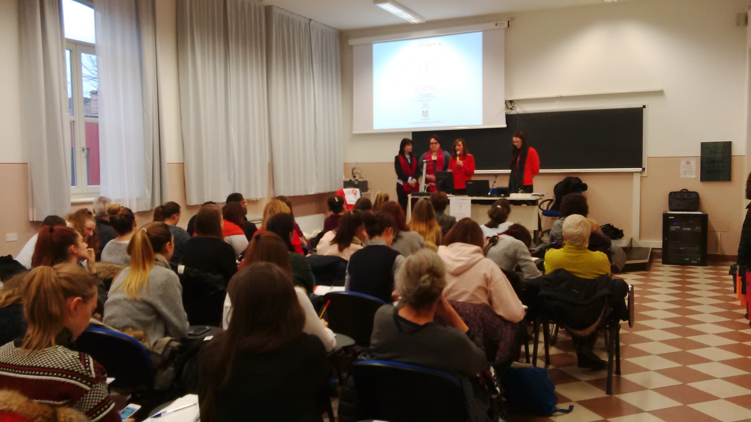 Un'aula universitaria piena; in fondo tre relatrici accanto alla proiezione.