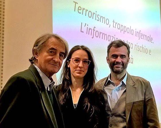 Tre persone in posa davanti alla proiezione del titolo dell'incontro sul terrorismo e l'informazione.