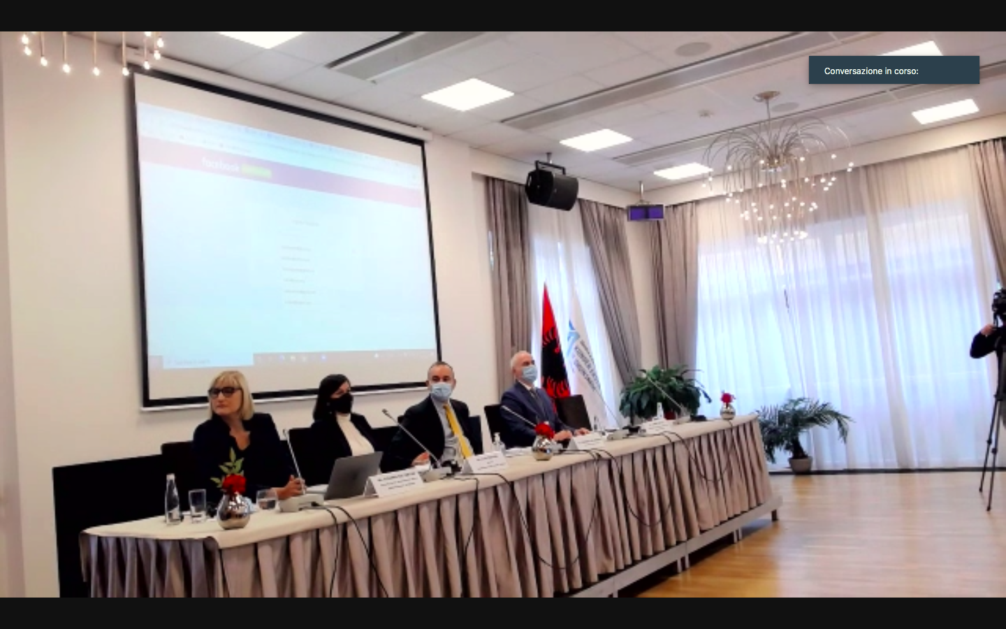 Il tavolo dei relatori con le mascherine, accanto alla bandiera albanese, ripreso durante il collegamento della conferenza.