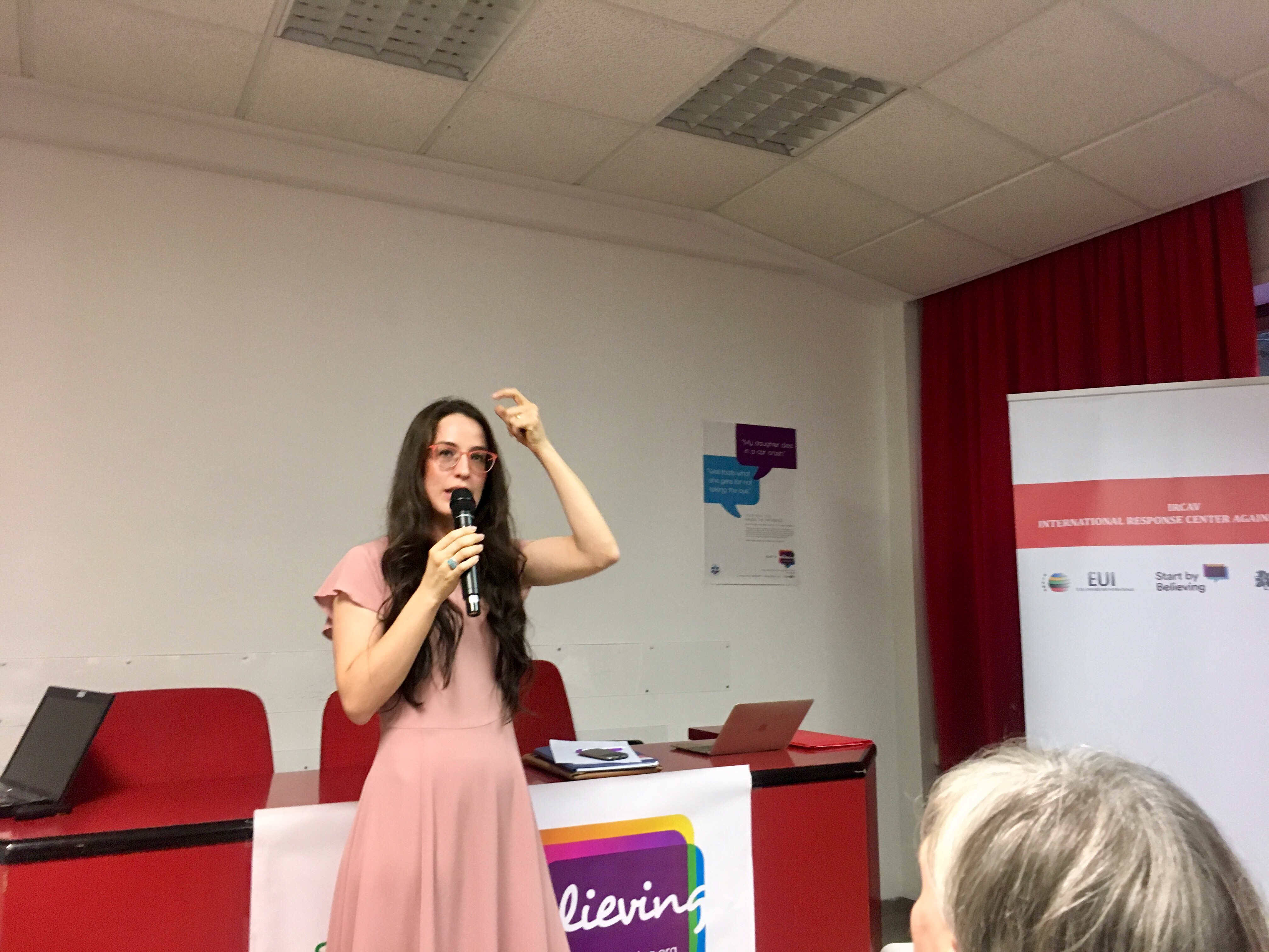 Una relatrice parla al microfono davanti al banner della campagna Start by Believing.