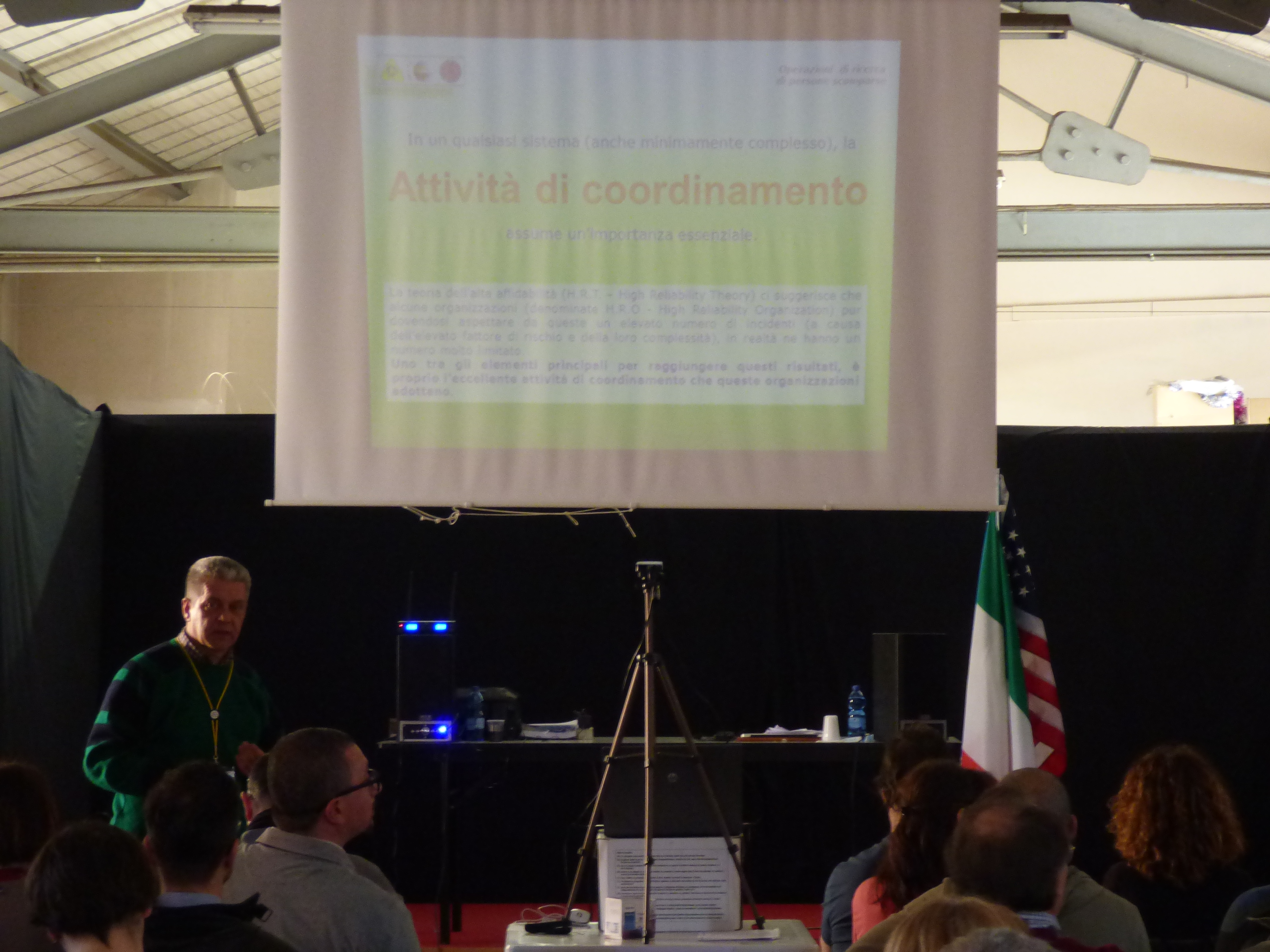 Un relatore accanto alla proiezione intitolata Attività di coordinamento, sotto un tendone.