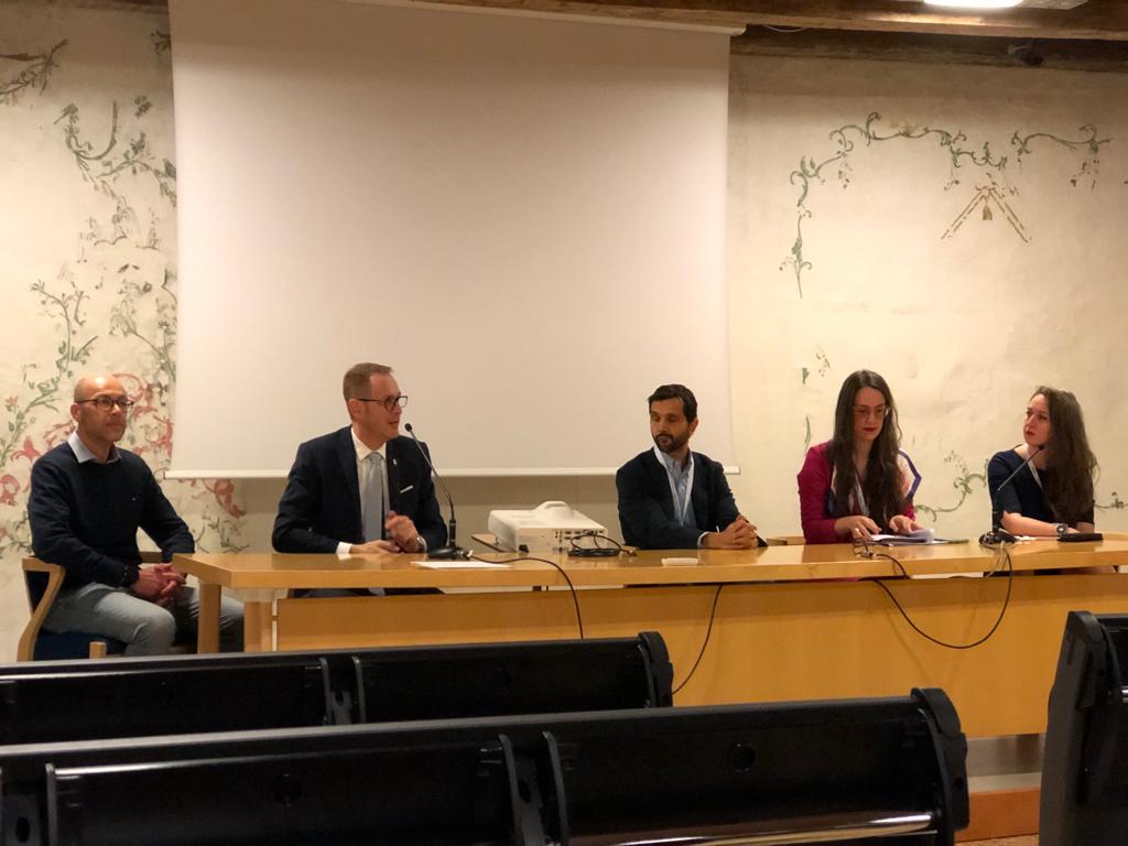 Cinque relatori al tavolo di un'aula affrescata.