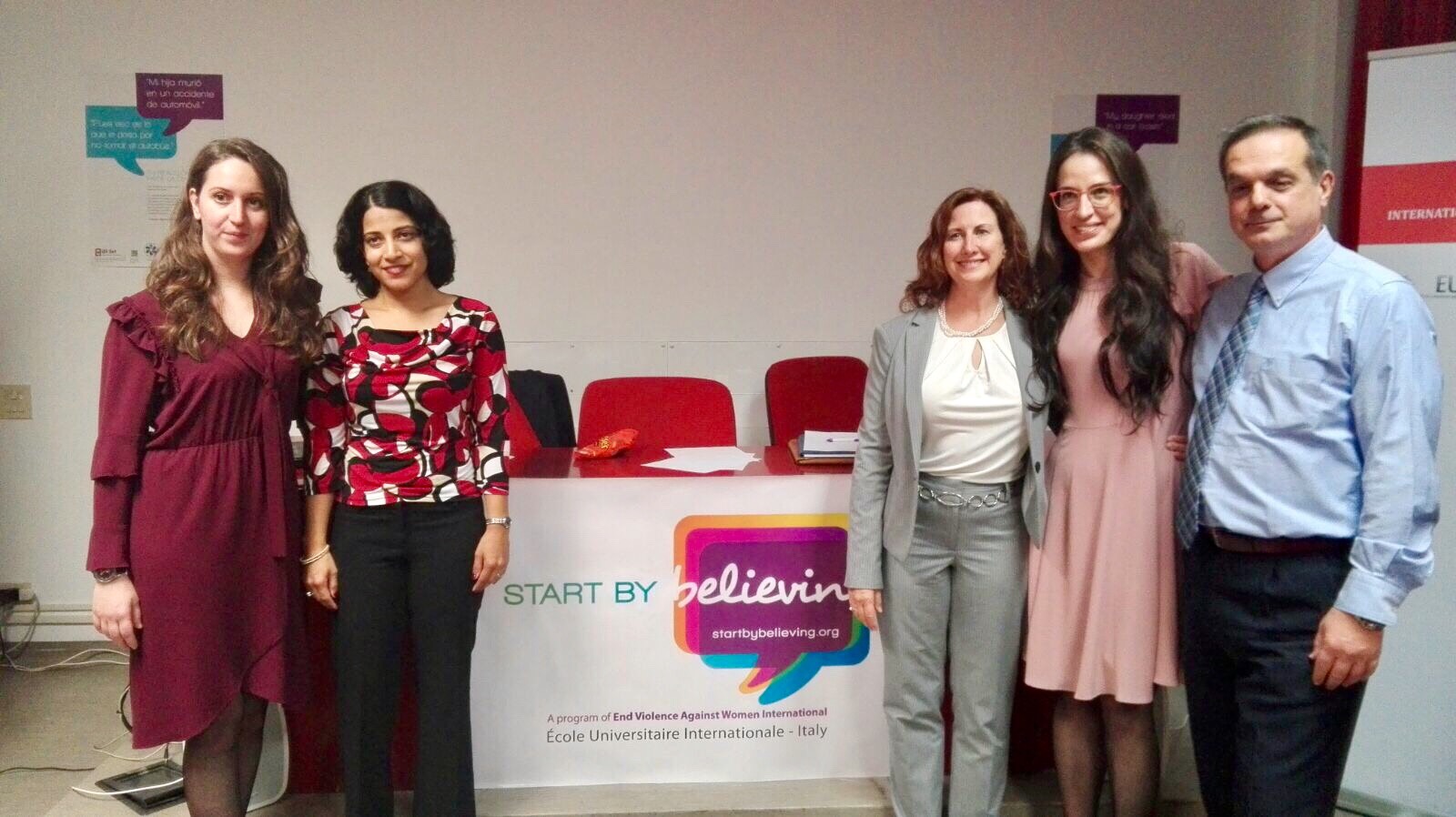 Cinque persone in posa davanti al banco con il logo della campagna Start by Believing.
