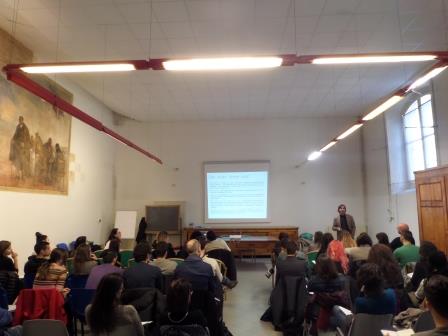 Il pubblico seduto in un'aula alta dalle travi rosse, davanti alla proiezione delle diapositive.