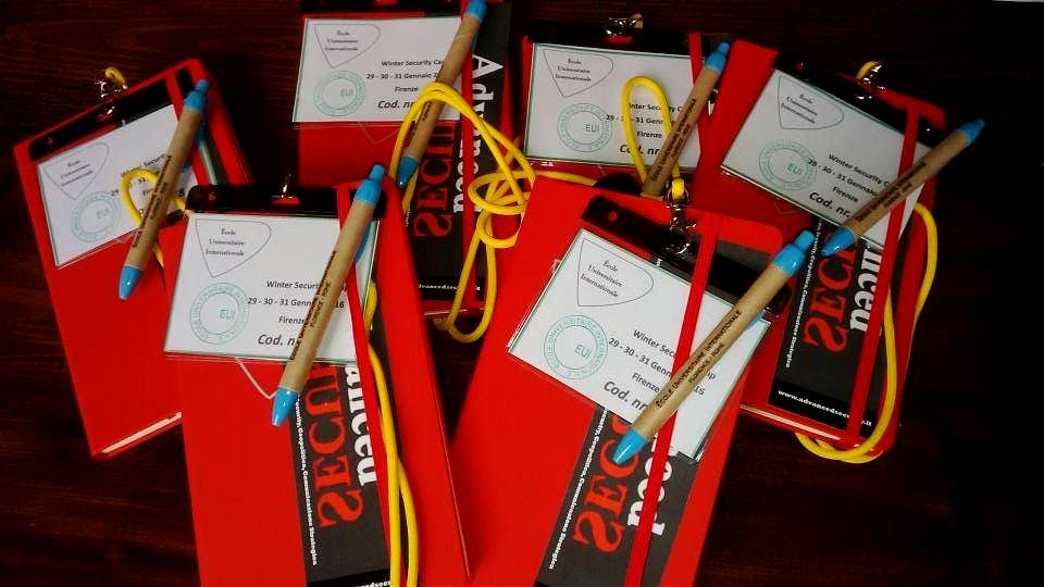 Il materiale dei partecipanti al Winter Security Camp: taccuini rossi, badge con il cordino e penne.