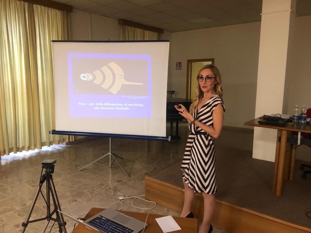 Una relatrice accanto alla proiezione di una diapositiva con l'icona di un'antenna che trasmette.