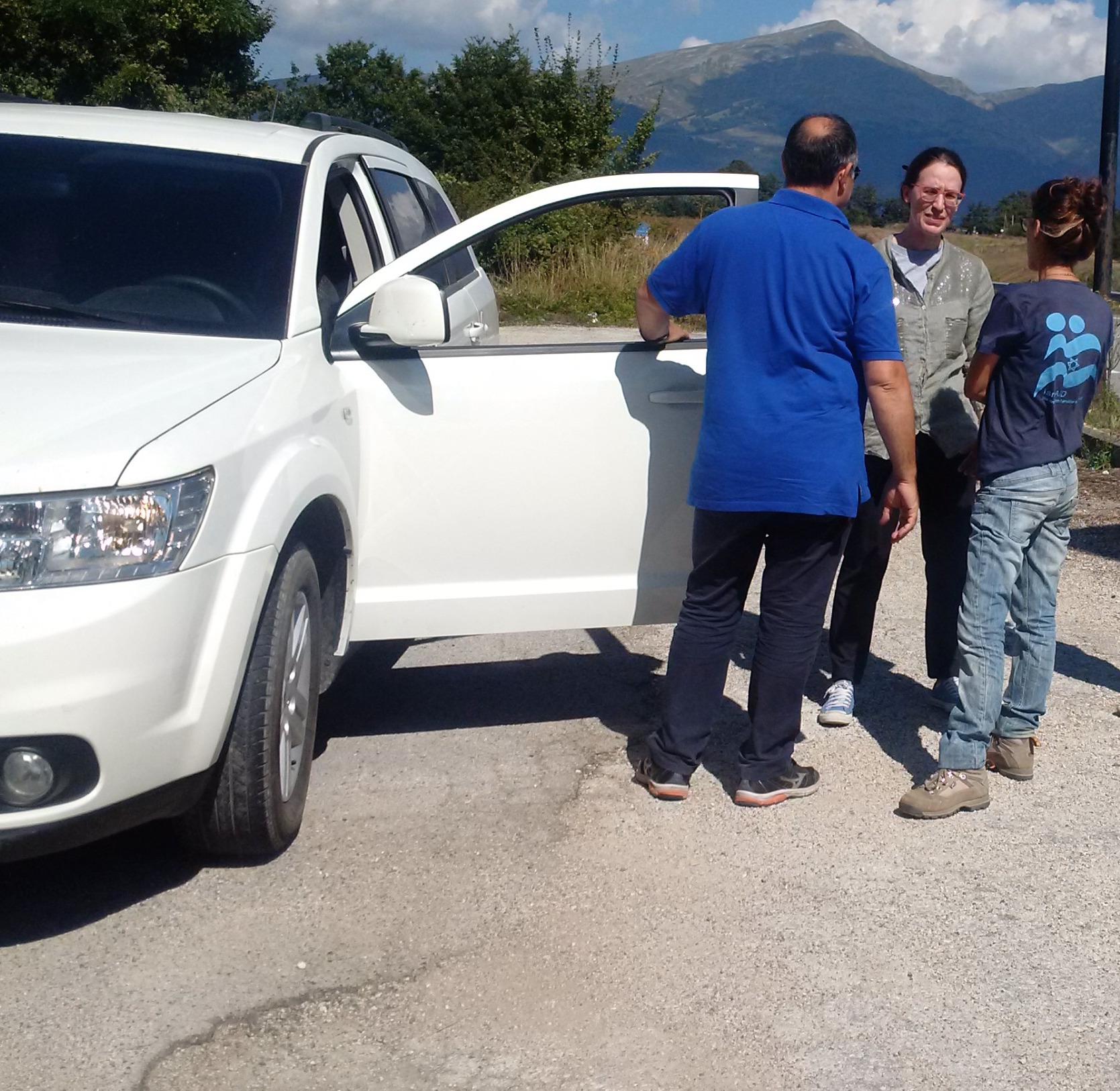 Tre persone accanto a un fuoristrada bianco su una strada di montagna, durante un'esercitazione.